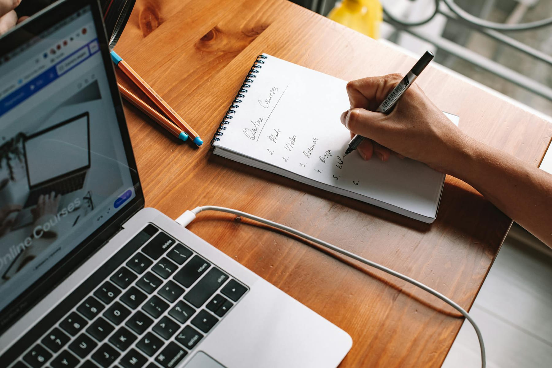 A person writing notes while researching online courses on a laptop in a home setting. on Skill Forge
