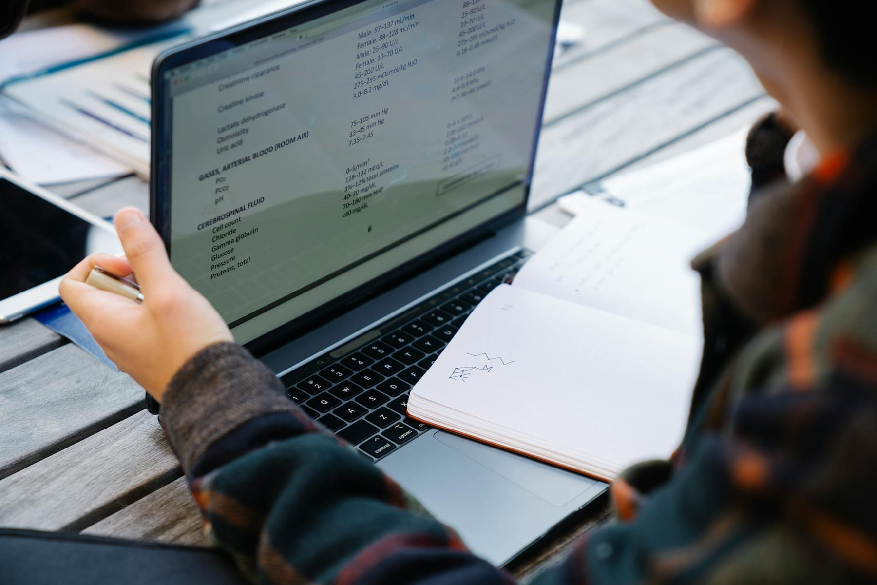 Close-up of hands using a laptop and taking notes at a wooden table. on Skill Forge