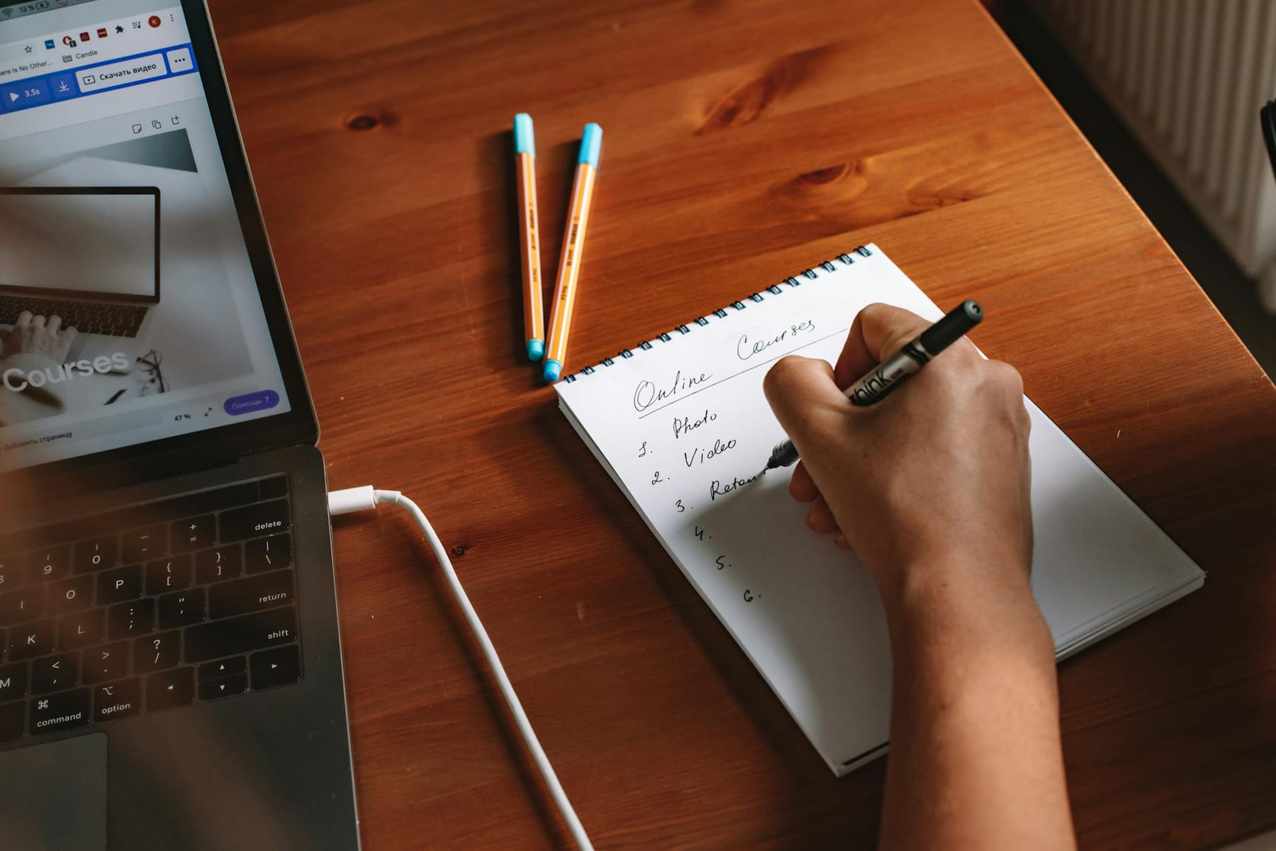 Photo of a person writing a list of online courses on a notepad next to a laptop. on Skill Forge