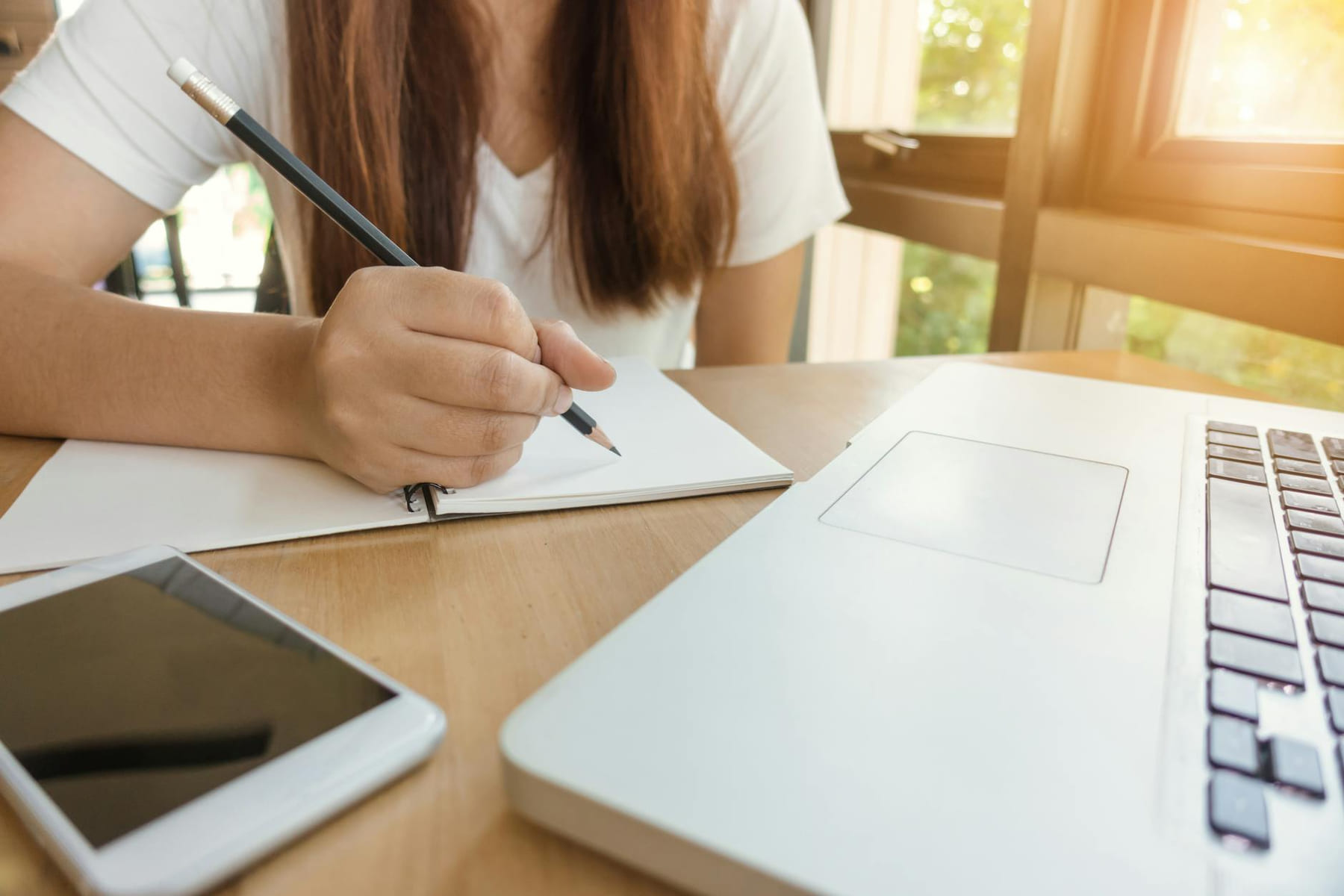 A young woman writing notes at a table with laptop and smartphone. on Skill Forge