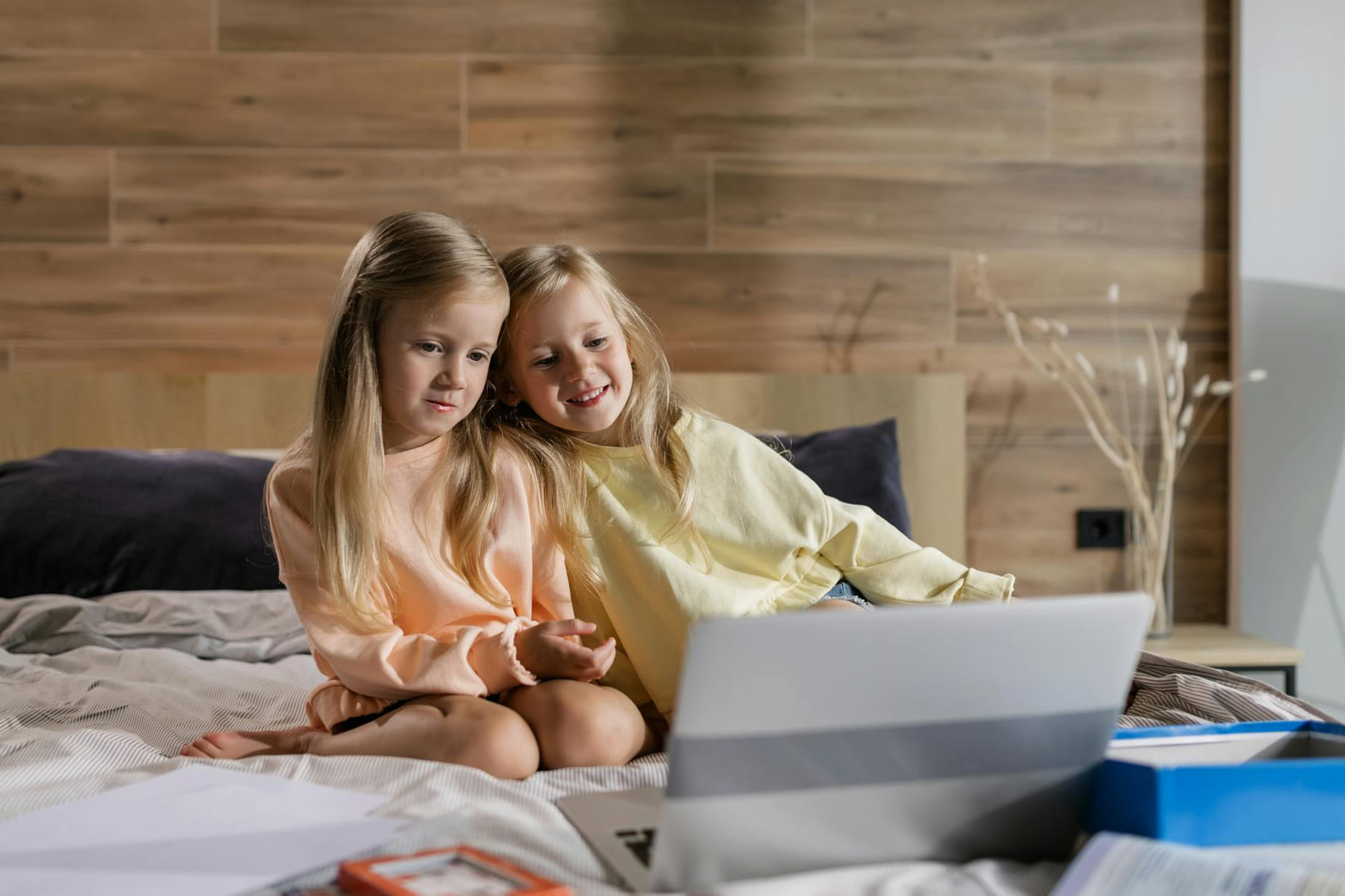 Two young girls sitting on bed, engaging in online learning using a laptop at home. on Skill Forge