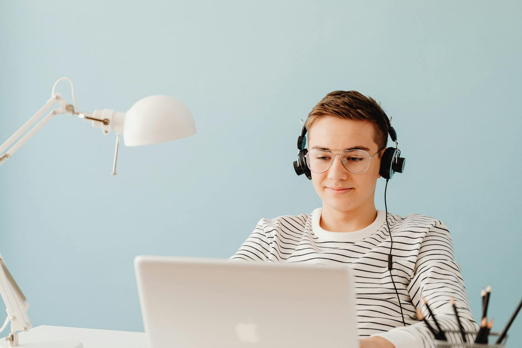 Teenager with headphones working on laptop in home office, exemplifying remote learning. on Skill Forge
