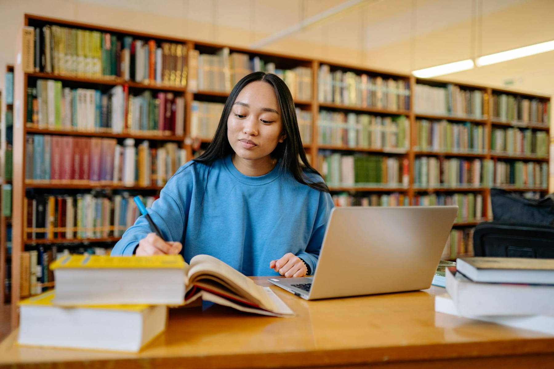 Young woman studying in a library with books and laptop, focusing on education. on Skill Forge