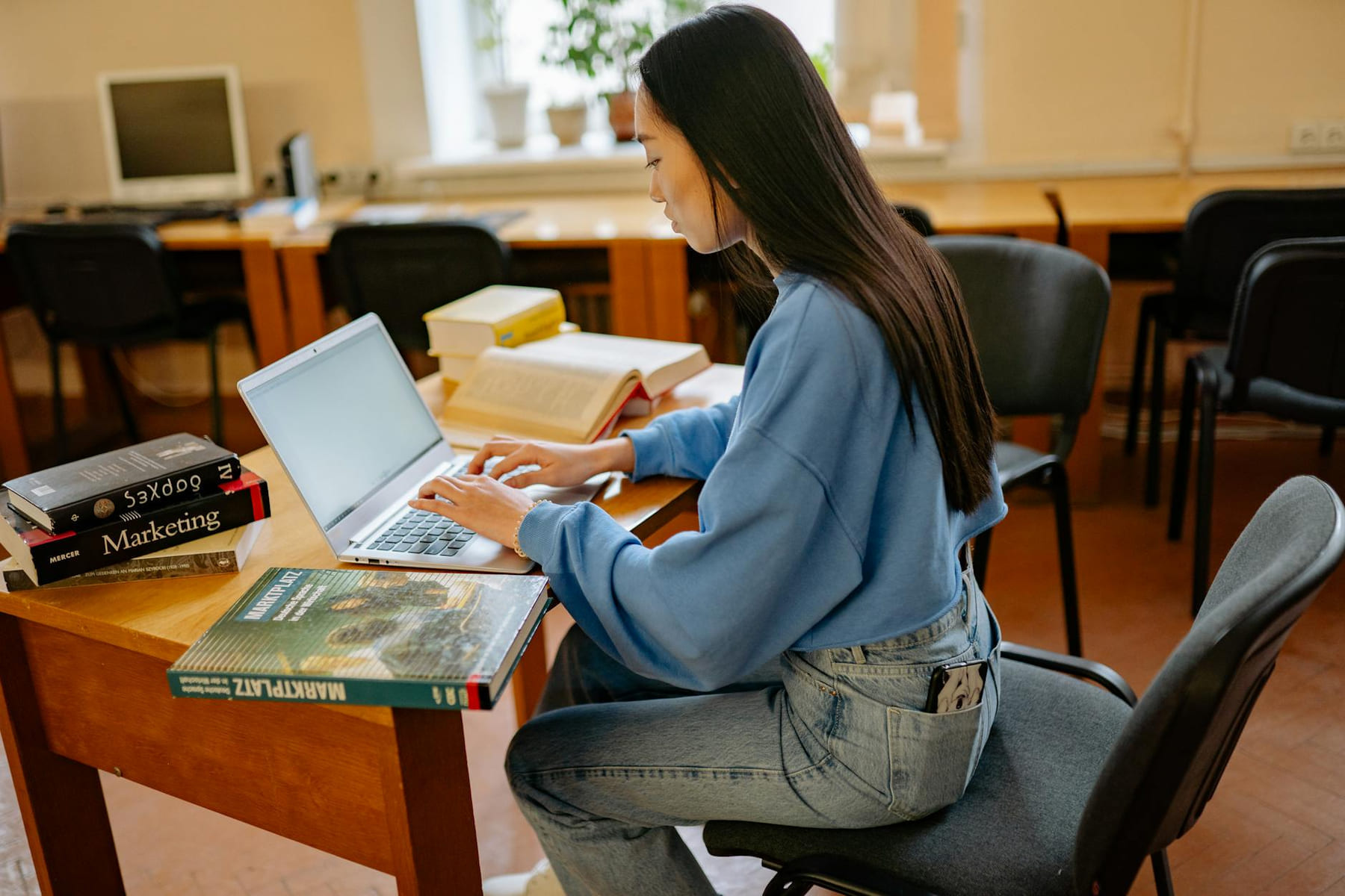 Focused woman typing on laptop, surrounded by books in a cozy study spot. on Skill Forge