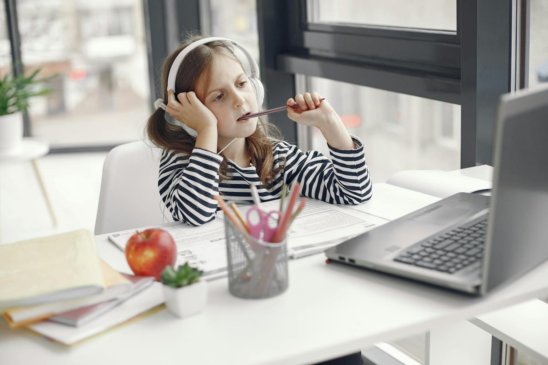 A child wearing headphones doing homework on a laptop indoors. Remote learning setup. on Skill Forge