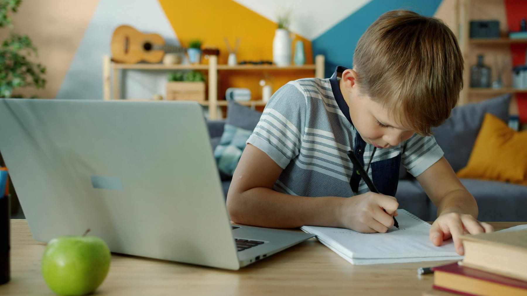 Young boy writing notes at home using a laptop for learning. on Skill Forge