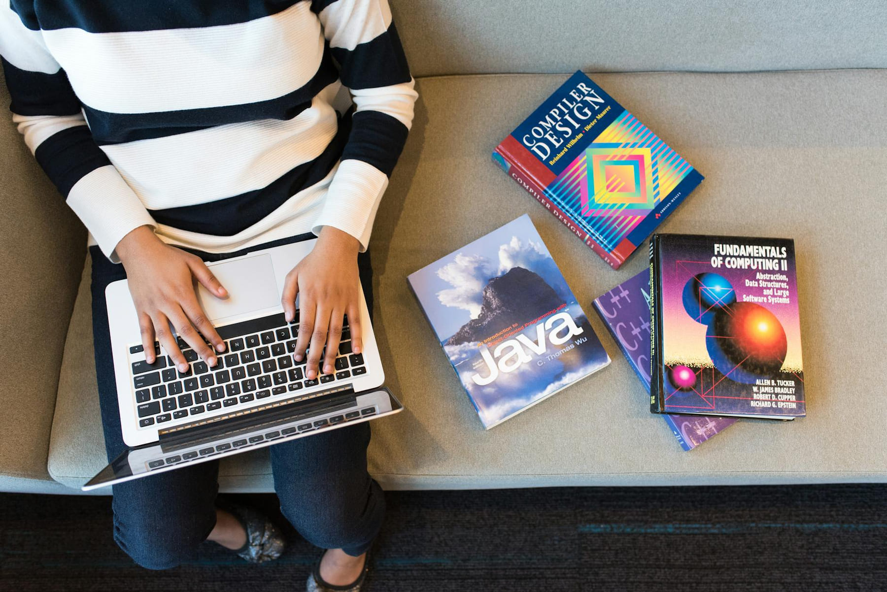 Woman using laptop on sofa, surrounded by programming books, learning coding. on Skill Forge