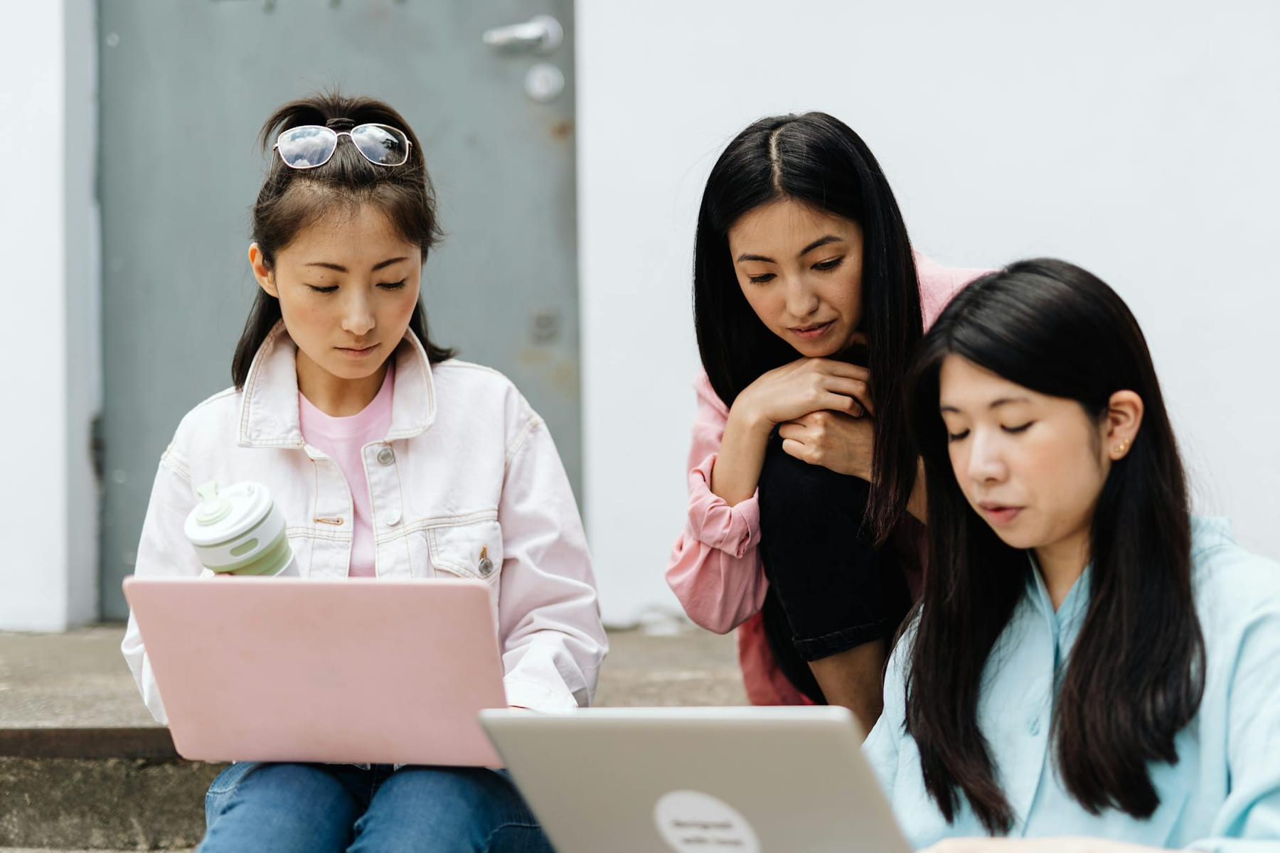 Three young Asian women working together on laptops outdoors, highlighting education and technology. on Skill Forge