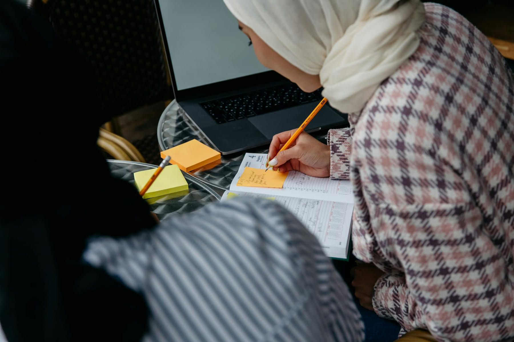 Muslim woman in hijab writing notes at café table with laptop and planner. on Skill Forge