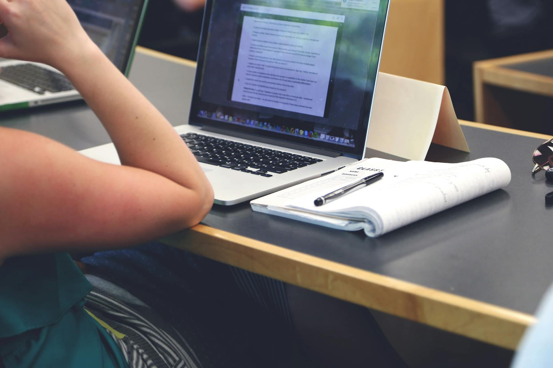 A student in a classroom setting using a laptop and taking notes in a notebook. on Skill Forge