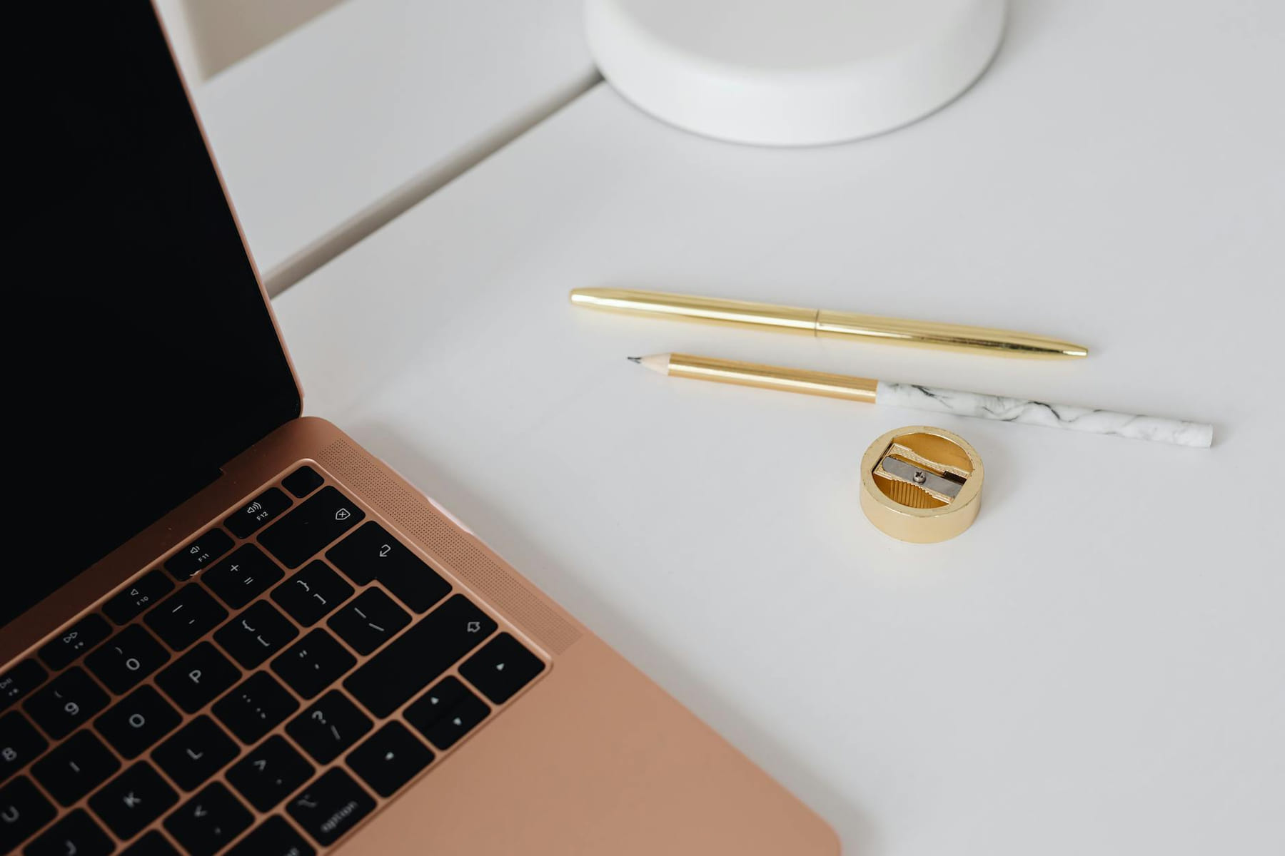 Elegant workspace featuring a gold pen, marble pencil, sharpener, and laptop on a white desk. on Skill Forge