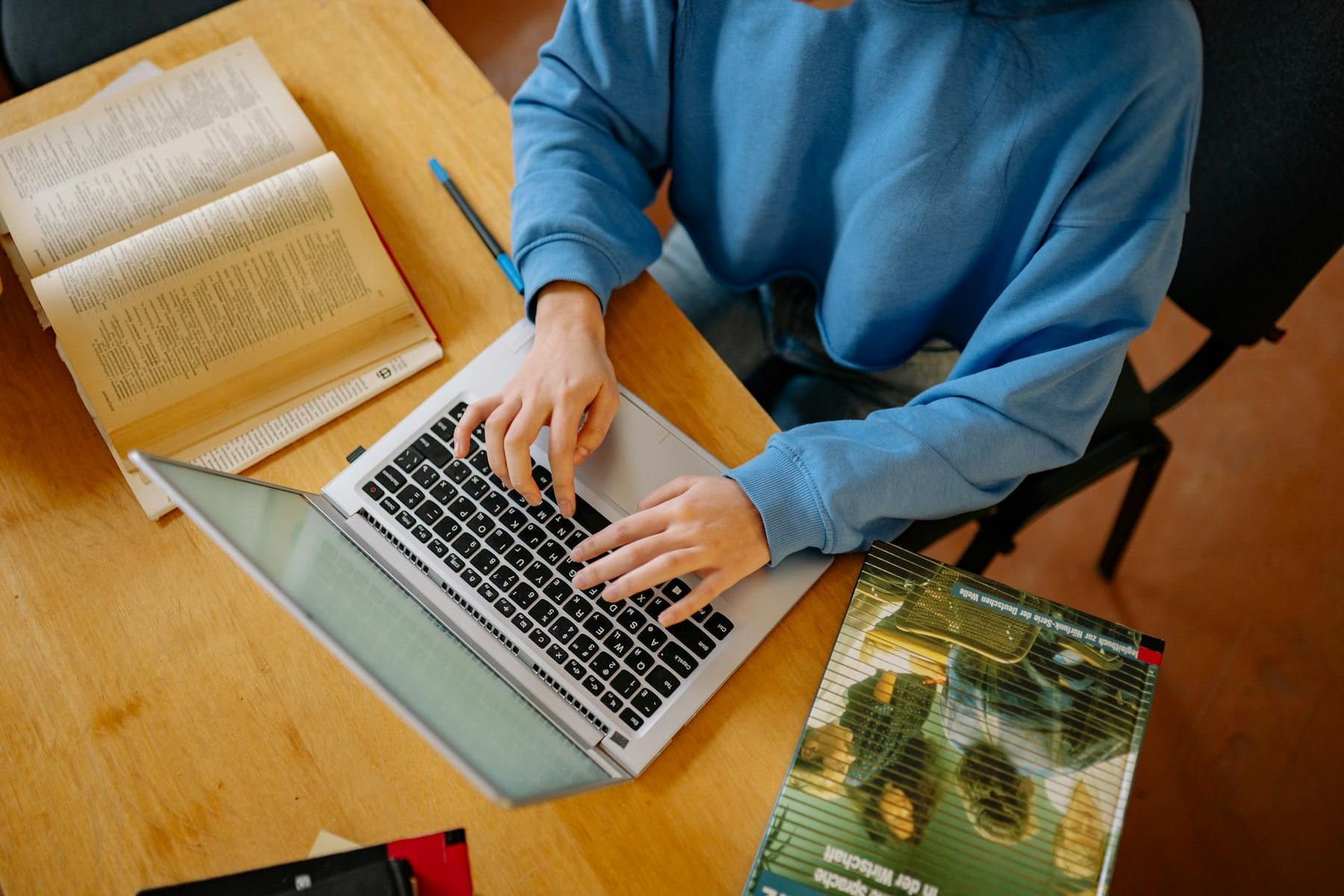 A student typing on a laptop surrounded by open books, focusing on research and school work. on Skill Forge